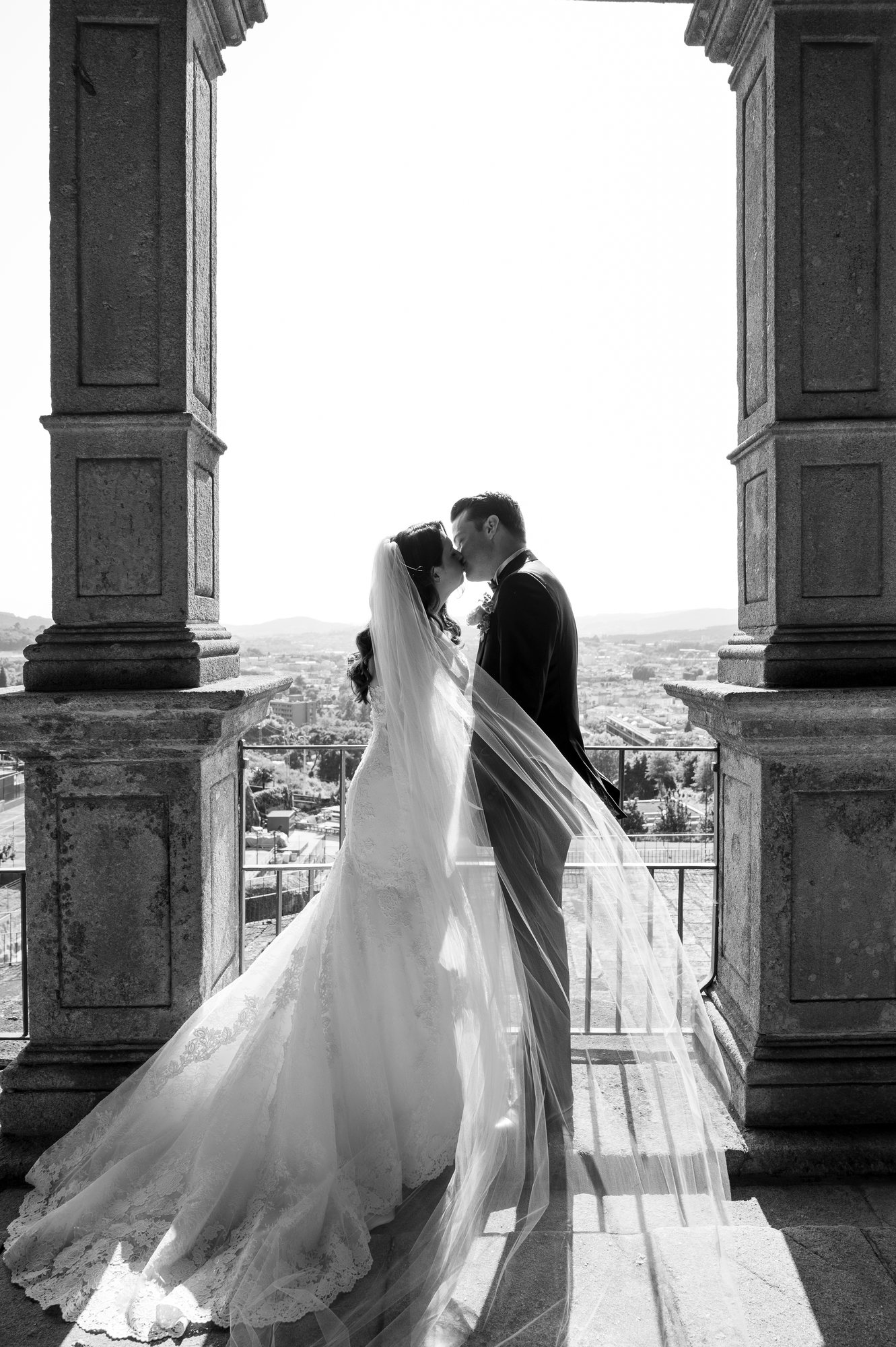 Couple kissing between stone columns, her long veil trailing behind